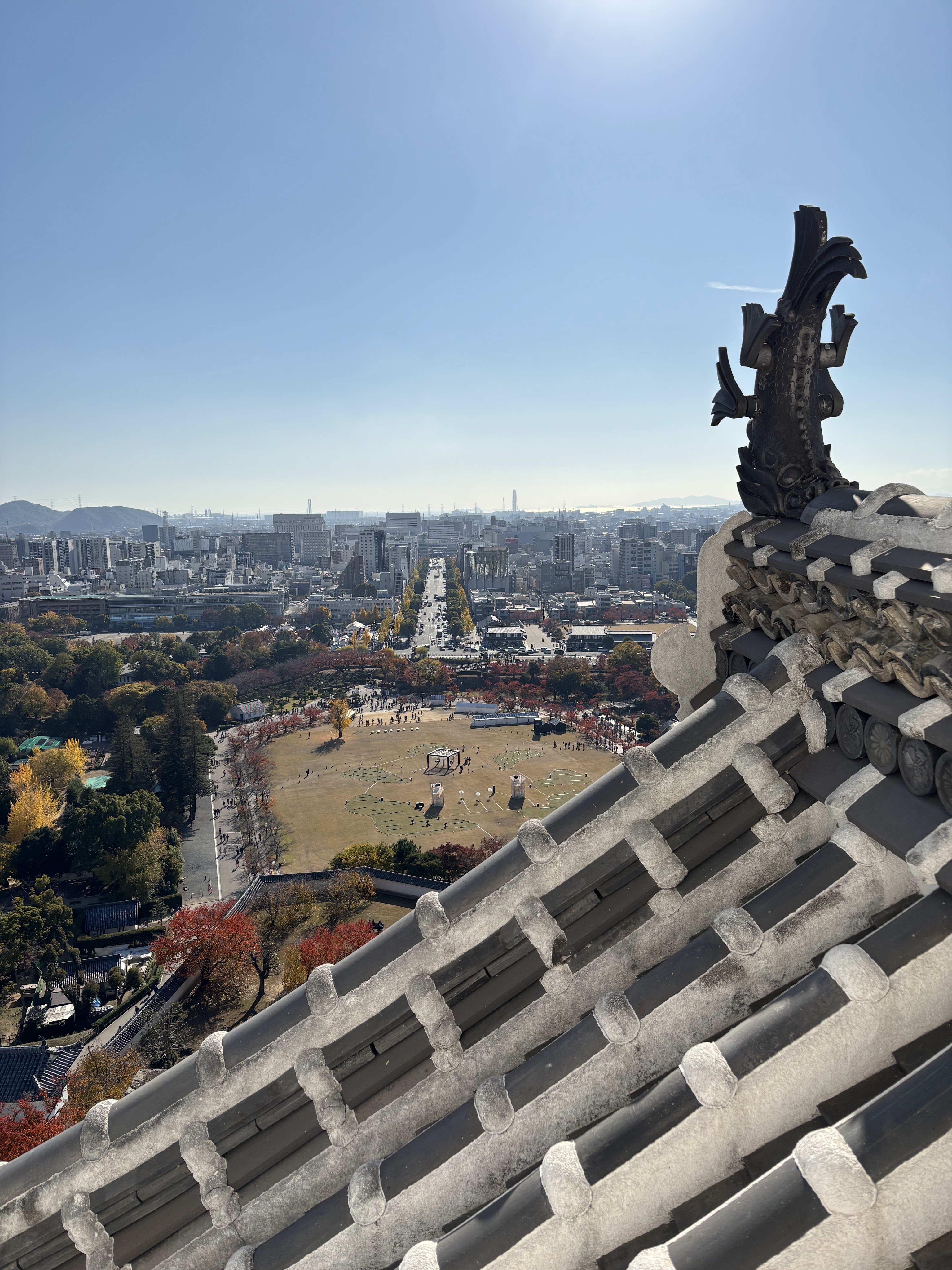 View from the top of Himeji Castle overlooking the city, with roof tiles and autumn trees in the foreground.